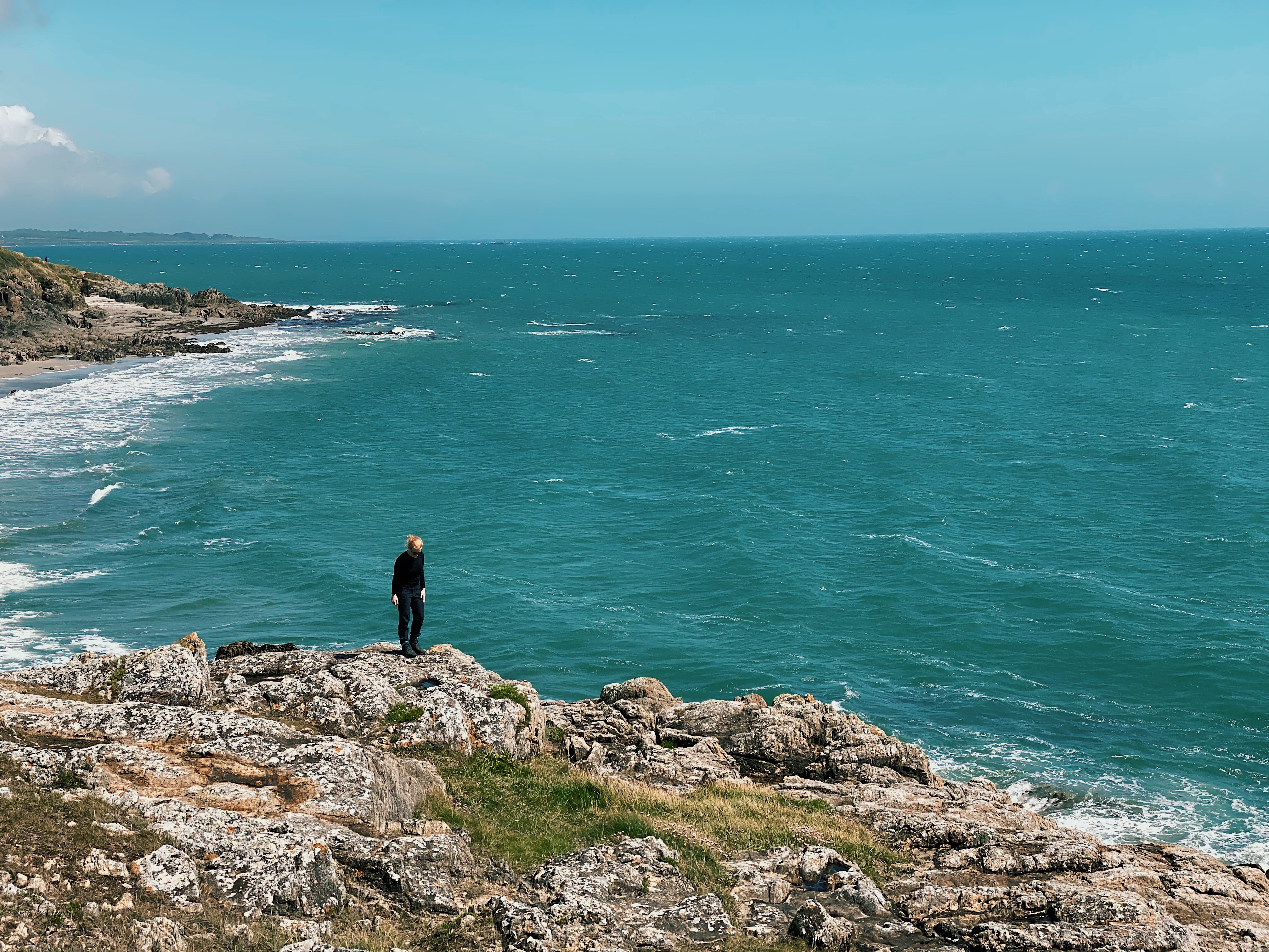 View of a woman standing on rough cliffs in Brittany, France in front of the open sea