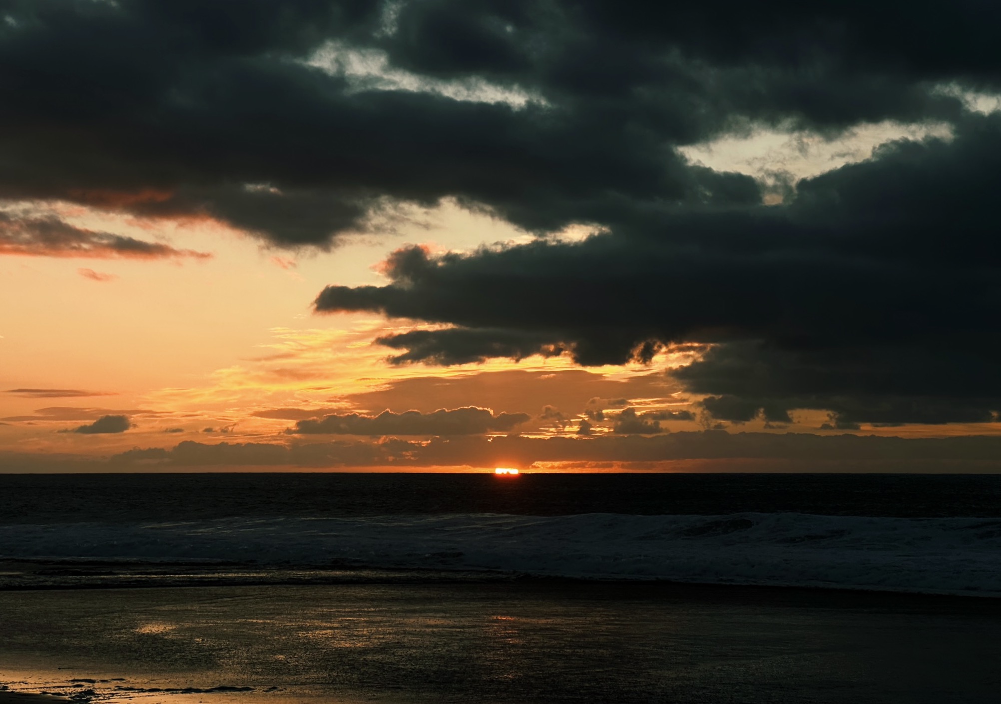 Sun setting over the dark sea with several dark clouds and a deep orange sky while hiking on Fuerteventura, Canary Islands, Spain